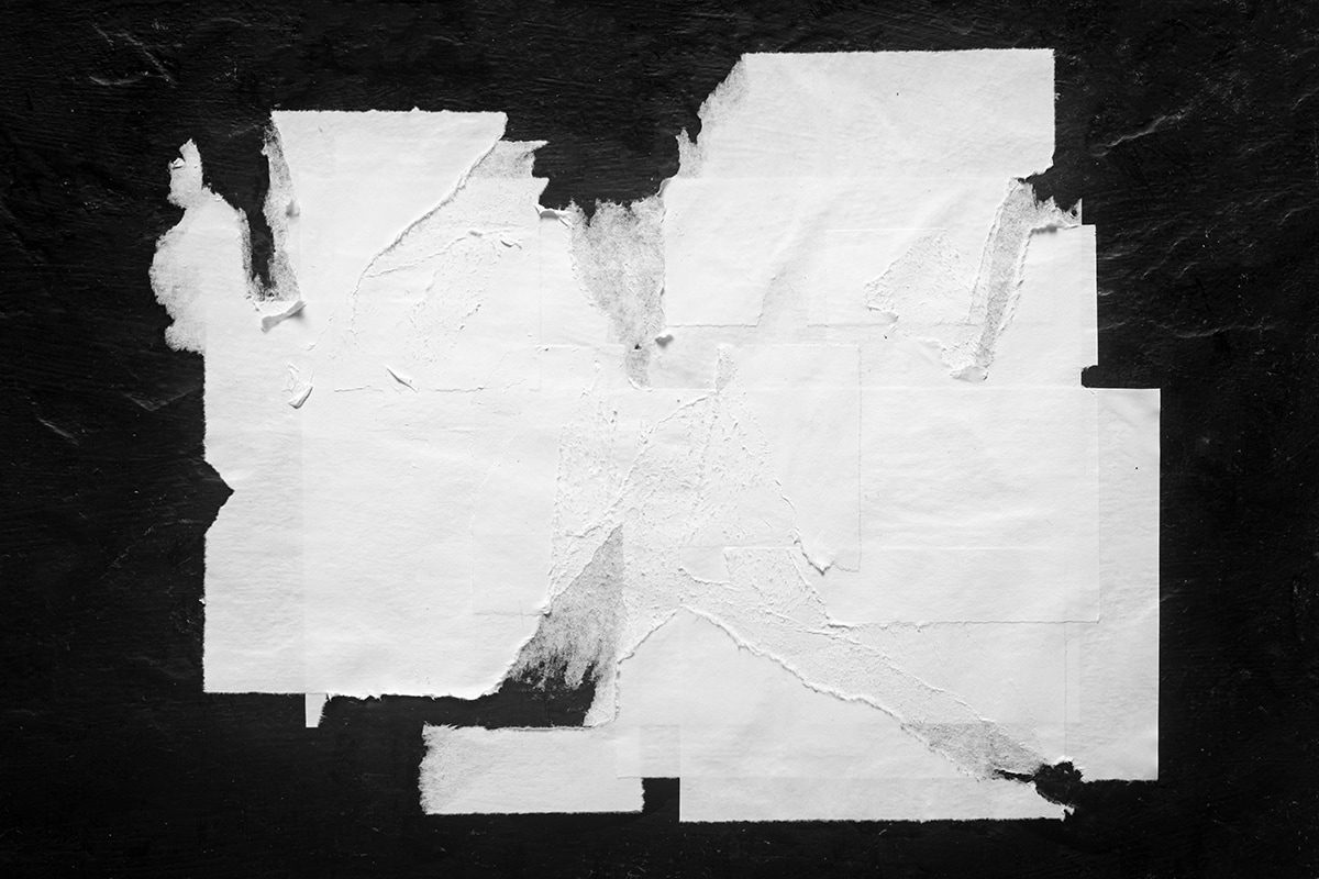 Overlapping pieces of torn white paper lie on a textured black surface.