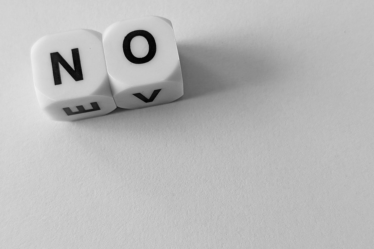 Two white letter cubes spell "NO" and cast shadows on a pale surface.